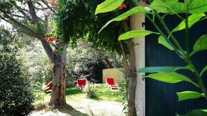 Un jardín con un camino de grava, dos sillas rojas y un cobertizo azul.
