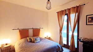 Un dormitorio con una cama, dos lámparas de noche, un ventanal con cortinas y un colgador de techo.