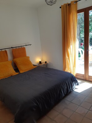 A bedroom with a bed, two pillows, a nightstand, a lamp, and a window with curtains. - Suite with private garden Aix-Luberon-Verdon * Dinner and Jacuzzi extra (Peyrolles-en-Provence)