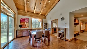 A spacious dining area with a wooden table and chairs, large windows, and a view of trees outside. - Luxury Penthouse Condo (Sun Peaks)