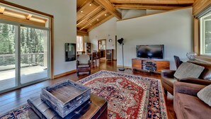 A spacious living room with a large wooden ceiling, a television, a sofa, and a patterned rug. - Luxury Penthouse Condo (Sun Peaks)