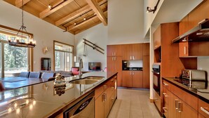 A modern kitchen with wooden cabinets, stainless steel appliances, and a large island with a dishwasher. - Luxury Penthouse Condo (Sun Peaks)