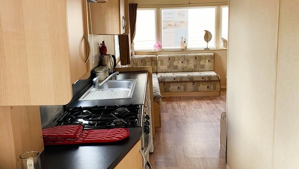 A compact kitchen with a gas stove, a sink, and a window with a view of the outside. - Beautiful 3-bedroom Caravan at Mersea Island (Colchester)