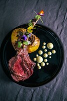 Un plato con un filete a la parrilla, una papa asada y algunas guarniciones.