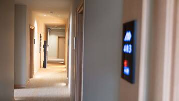 A hotel hallway with a carpeted floor, a door on the left, and a digital display on the right.