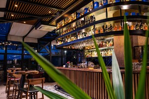 A bar area with shelves of liquor bottles and glasses, wooden chairs, and a modern ceiling design. - Avec Hotel (Çanakkale)