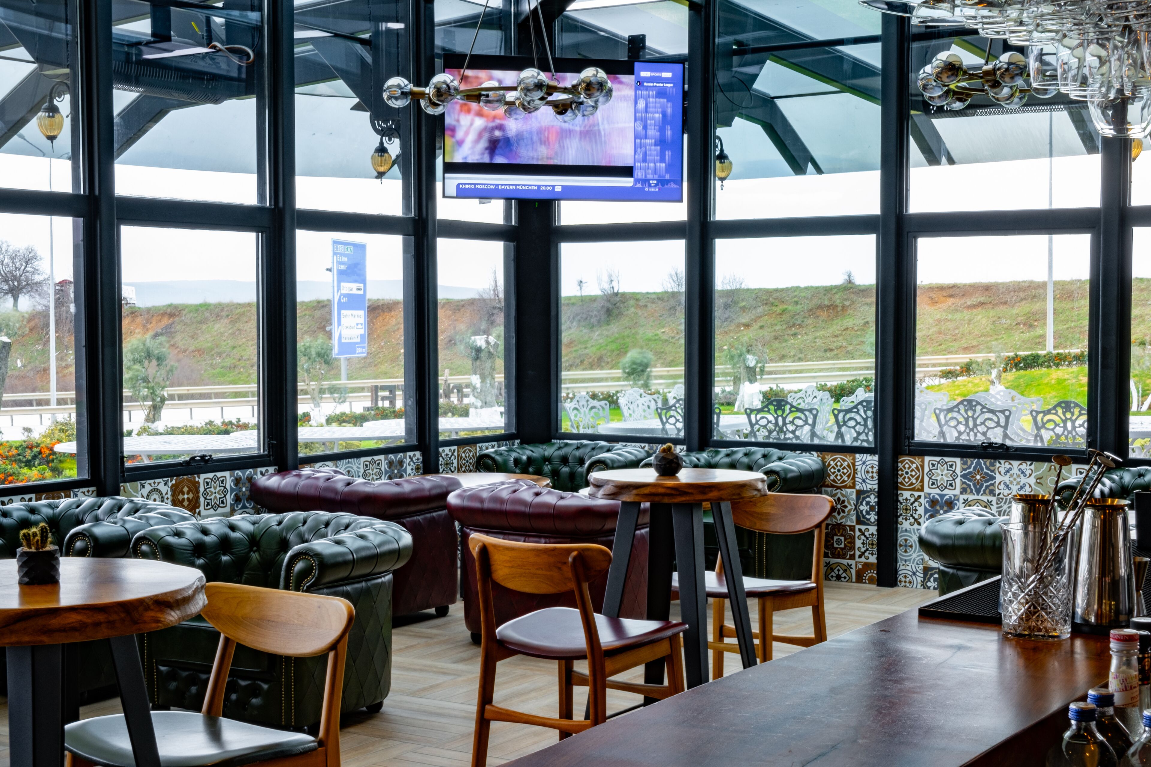 A modern bar area with leather seating, a wooden bar counter, and a large window offering a view of the outdoors.