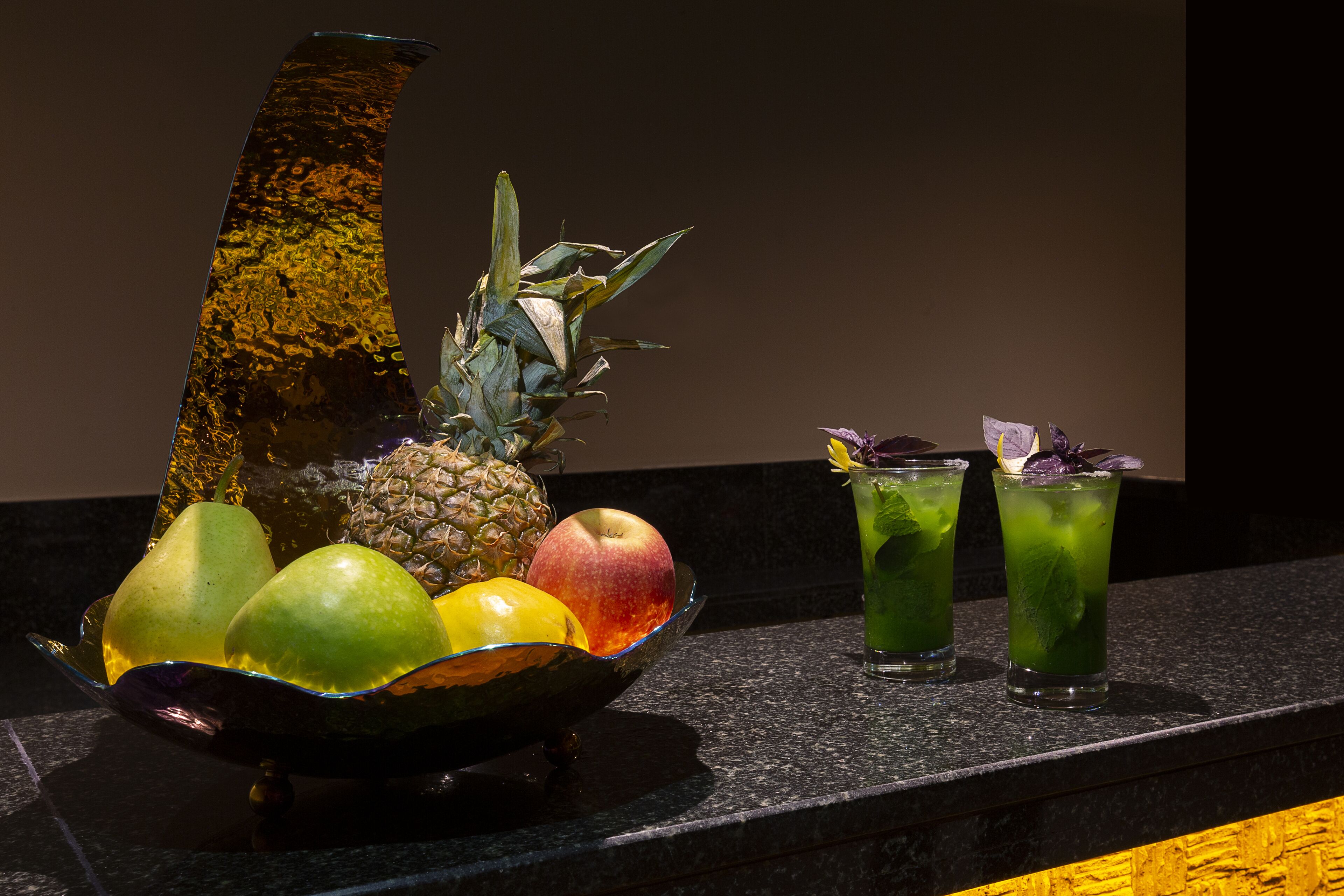 A fruit bowl with pears, an apple, and a pineapple on a countertop.