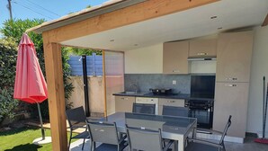 A modern outdoor kitchen with a dining area, including a table and chairs, and a red umbrella. - 3 bedroom house 90m² Hyères the sea is 50 meters from the beach (Hyères)