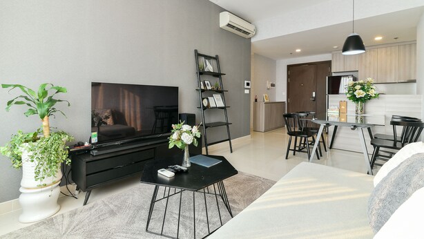 A modern living room with a flat-screen TV, a coffee table, and a dining area with a table and chairs. - Brian Rivergate Homes (Hồ Chí Minh)
