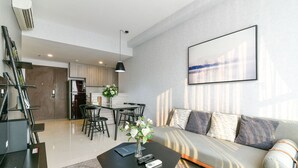 A modern living room with a sofa, a coffee table with a vase and remote controls, and a dining area in the background. - Brian Rivergate Homes (Hồ Chí Minh)
