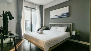 A modern hotel room with a large bed, a desk with a computer, a view of the city through a large window, and a painting on the wall. - Brian Rivergate Homes (Hồ Chí Minh)