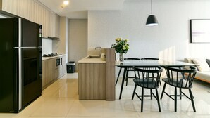 A modern kitchen with a built-in refrigerator, wooden cabinets, and a central island with a vase of flowers. There is a dining area with a table and chairs. - Brian Rivergate Homes (Hồ Chí Minh)