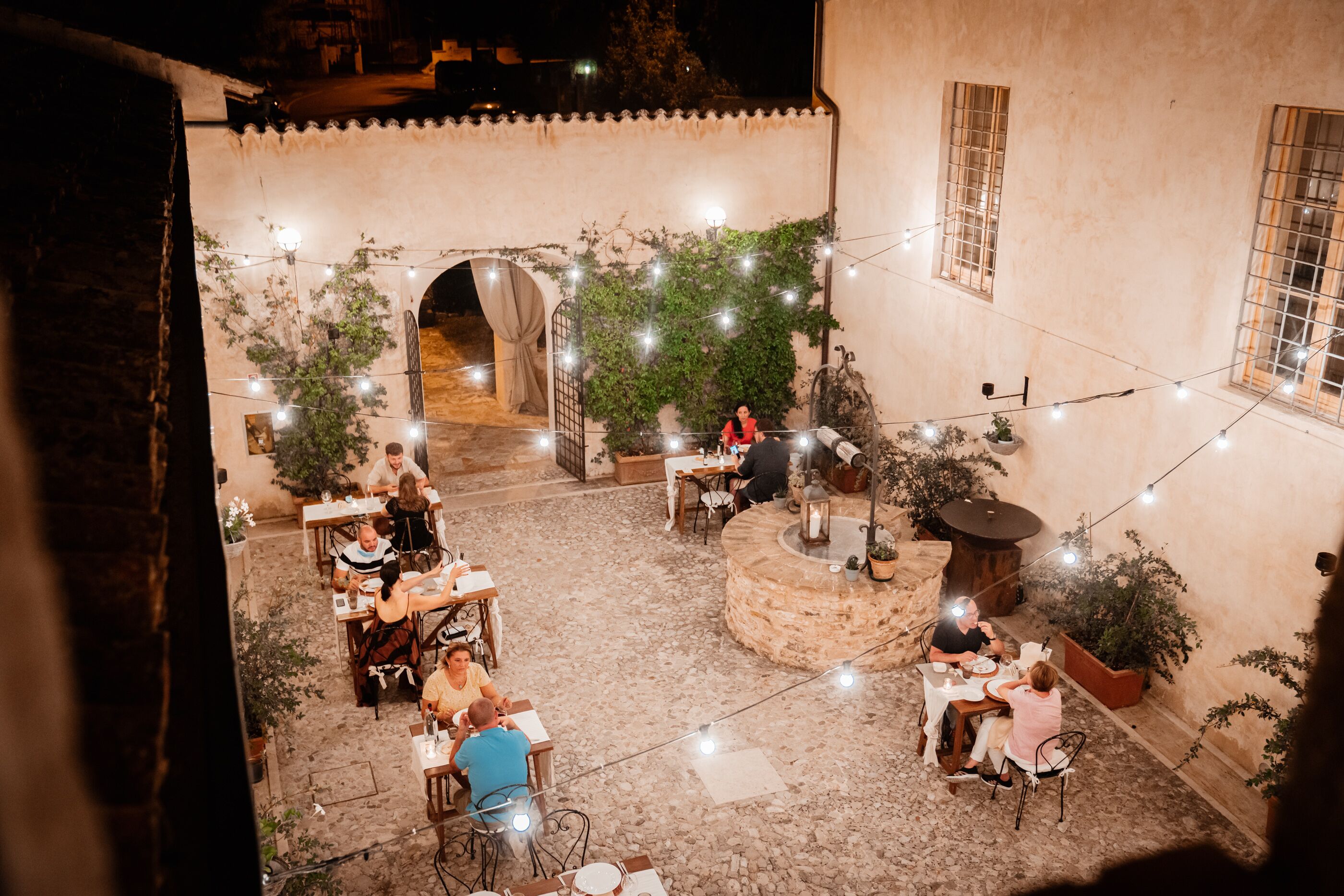An outdoor patio area with tables and chairs, string lights, and potted plants.