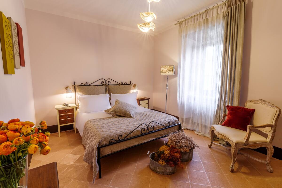 A bedroom with a bed, a chair, a nightstand, a lamp, and a vase with flowers.