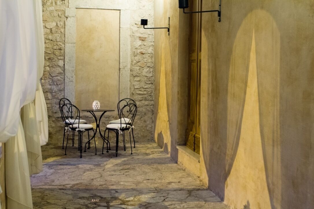 Une étroite ruelle pavée, avec une table et des chaises, un mur de pierre et une porte en bois.