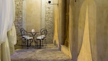 Une étroite ruelle pavée, avec une table et des chaises, un mur de pierre et une porte en bois.