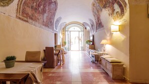 A hallway with a tiled floor, a table with a plant, a bench, and a lamp. - Relais Convento Santa Croce (Sant'Anatolia di Narco)