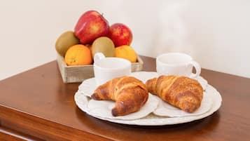 Une table en bois sur laquelle se trouve une assiette de croissants et un panier de fruits contenant des pommes, des oranges et des kiwis.