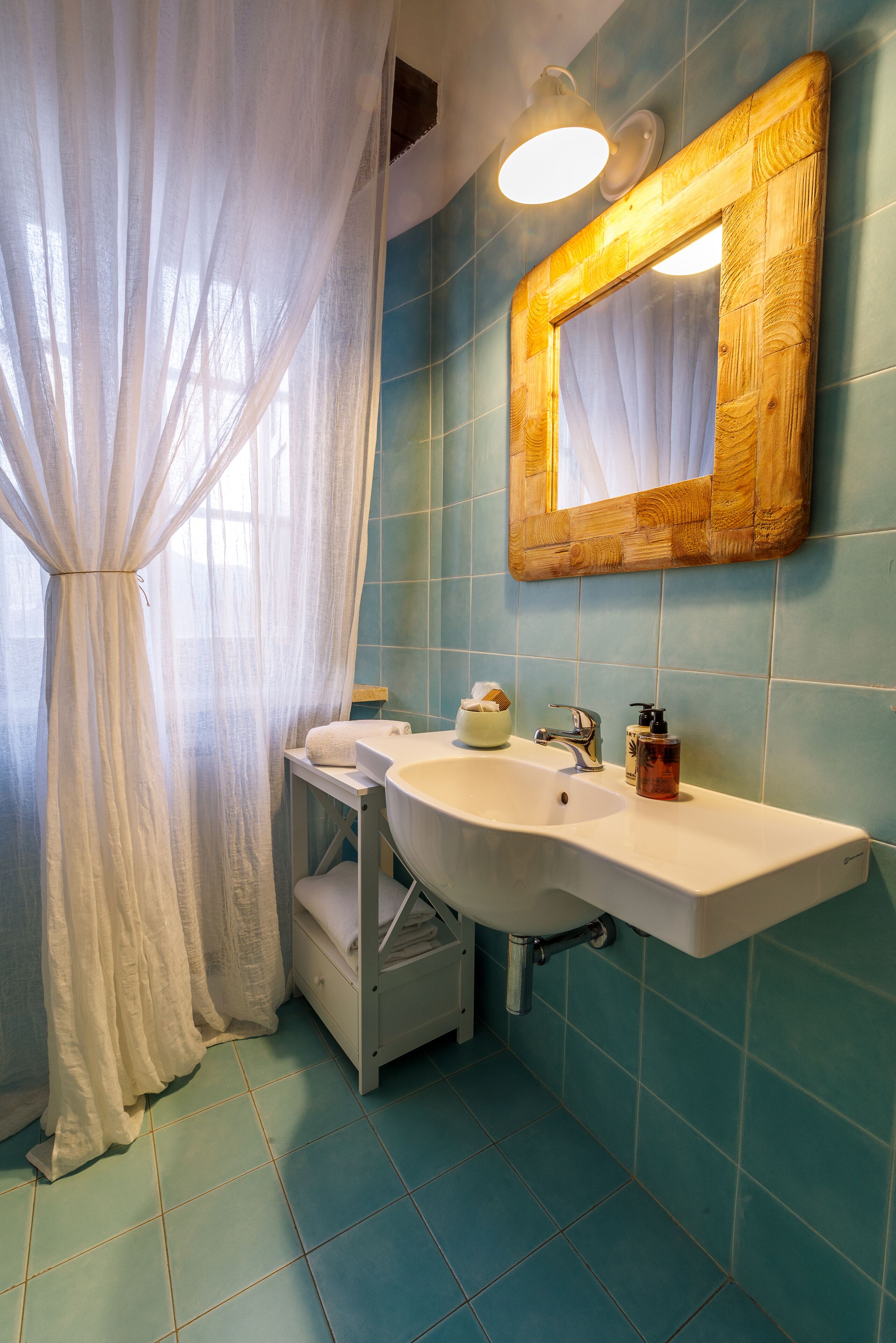 Een badkamer met een witte wastafel, een spiegel met houten lijst en een blauwe betegelde muur.