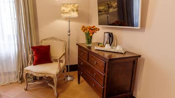 A room with a vintage chair, a wooden dresser, a vase of flowers, a floor lamp, and a painting on the wall.