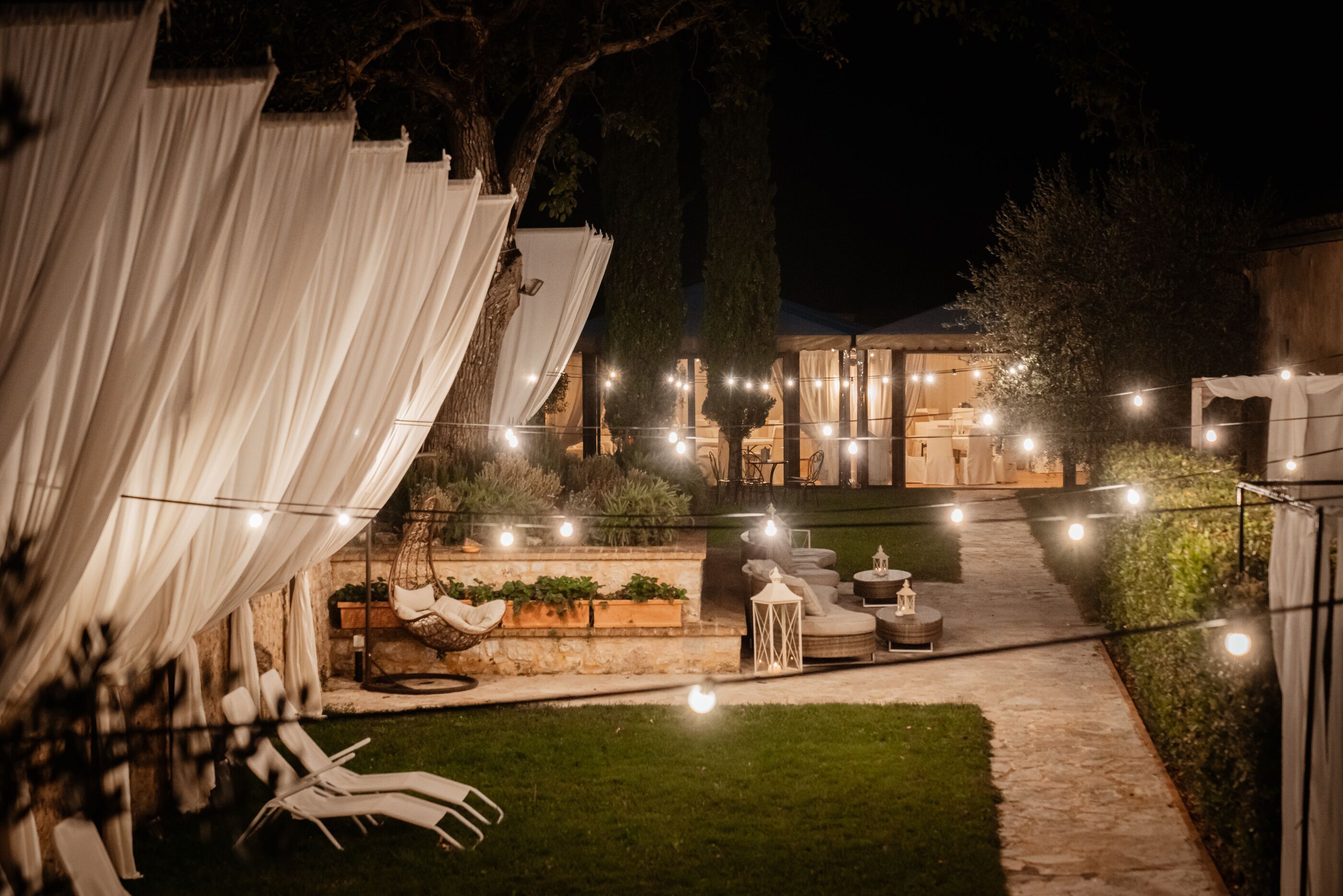 An outdoor patio area with string lights, white drapes, and seating arrangements.