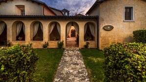 A building with a courtyard, arched doorways, and a stone pathway leading to an entrance. - Relais Convento Santa Croce (Sant'Anatolia di Narco)