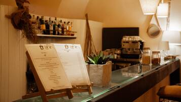 Un espace bar avec un tableau affichant le menu, des étagères remplies de bouteilles, une plante et une machine à café.