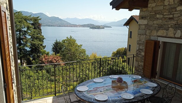 Een ronde tafel met stoelen op een balkon met uitzicht op een meer en bergen op de achtergrond.