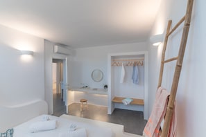 A modern hotel room with a large bed, a sitting area, a vanity with a mirror, and a wooden shelf.