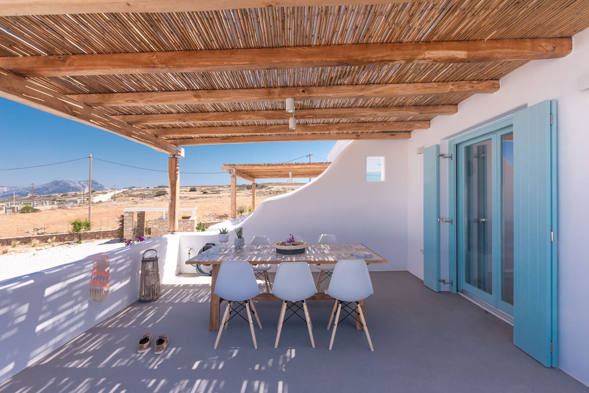An outdoor dining area with a table and chairs, a pergola overhead, and a view of the landscape.