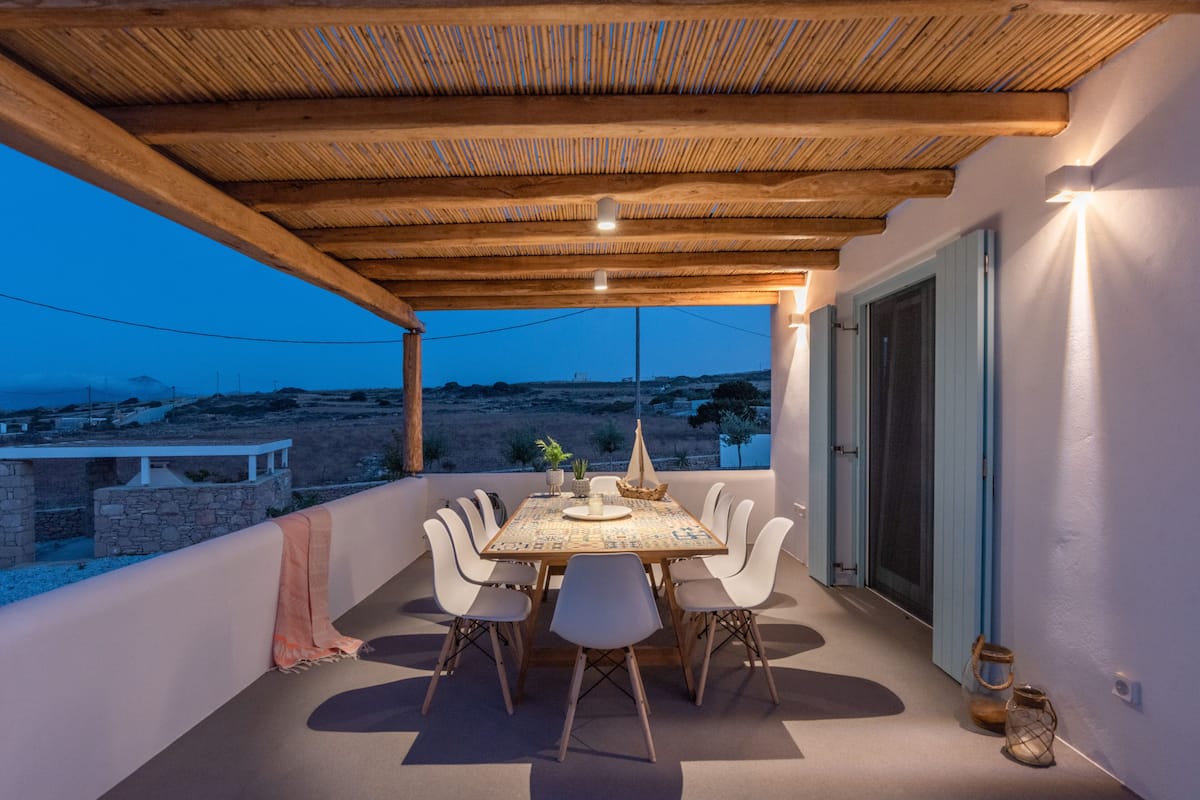 An outdoor dining area with a wooden table and chairs, a view of the landscape, and a pergola overhead.