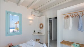 A bedroom with a bed, towels, a vanity with a mirror, a hanging light, and a view of the sea through a window. - Blue Harpist Villas (Naxos)