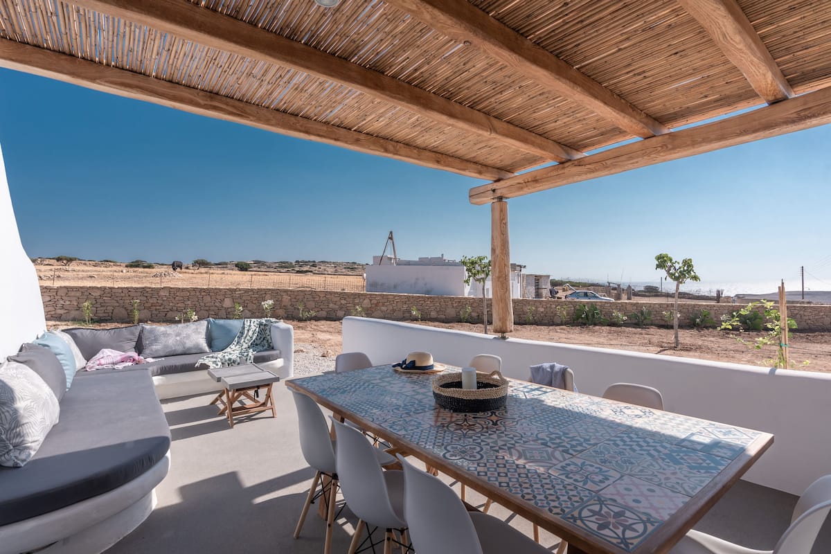An outdoor patio with a table and chairs, a sofa, and a view of the sea.