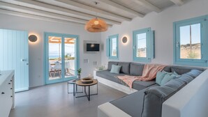 A modern living room with a grey sofa, a round table, and a hanging light fixture. - Blue Harpist Villas (Naxos)