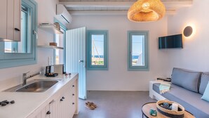 A modern kitchen with a sink, cabinets, and a dining area with a sofa and table. - Blue Harpist Villas (Naxos)