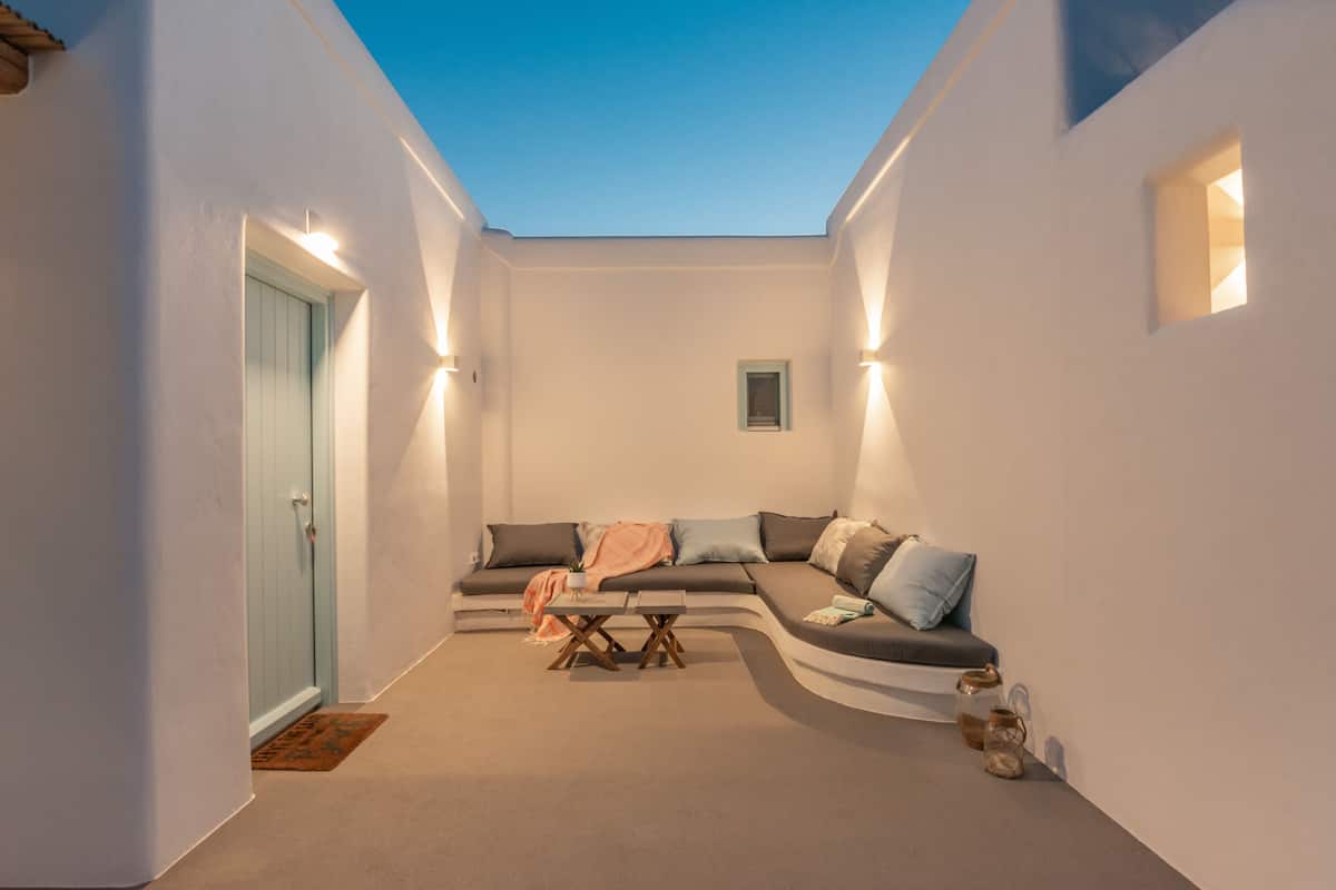 A cozy, well-lit living area with a curved sofa, a small table, and a door leading to another room.