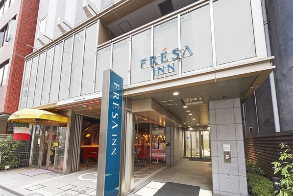 L’entrée d’un hôtel, avec une façade en verre transparent, une enseigne indiquant « FRESA INN » et une porte d’entrée bien visible.