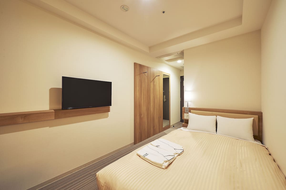 A hotel room with a bed, a television mounted on the wall, and a wooden wardrobe.