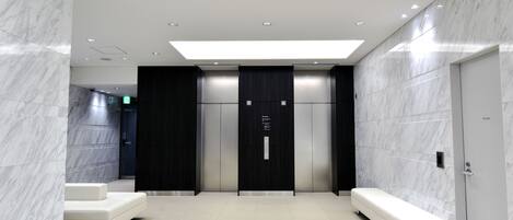 A modern elevator area with marble walls, a bench, and a digital display.