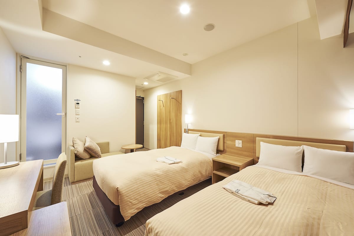 A hotel room with two beds, a desk, a chair, and a small table.