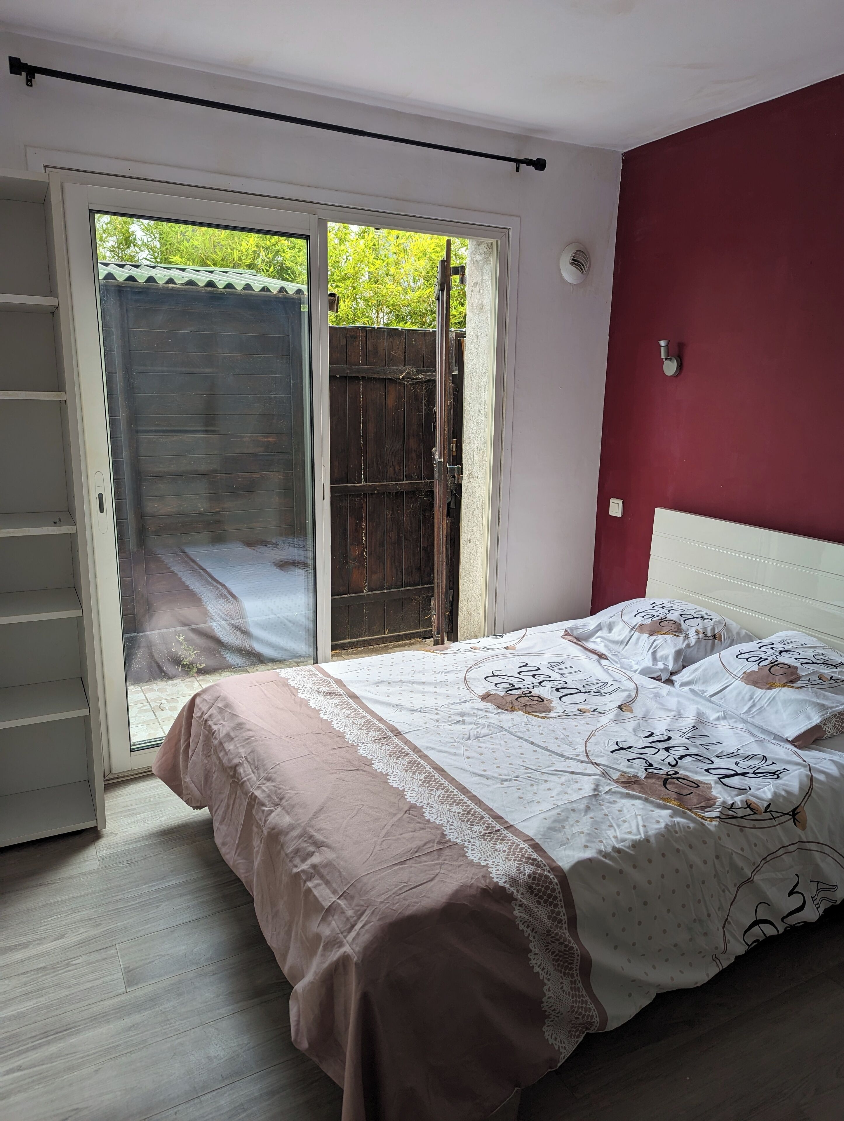 Un dormitorio con una cama, un cristalero corredizo que da a un patio y una pared roja.