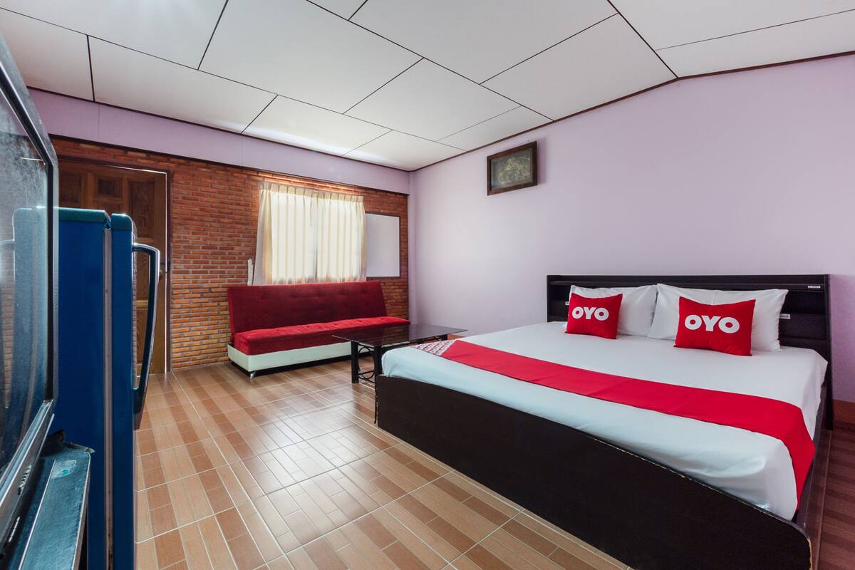Une chambre d’hôtel avec un lit, un canapé rouge, une petite table et une fenêtre avec des rideaux.