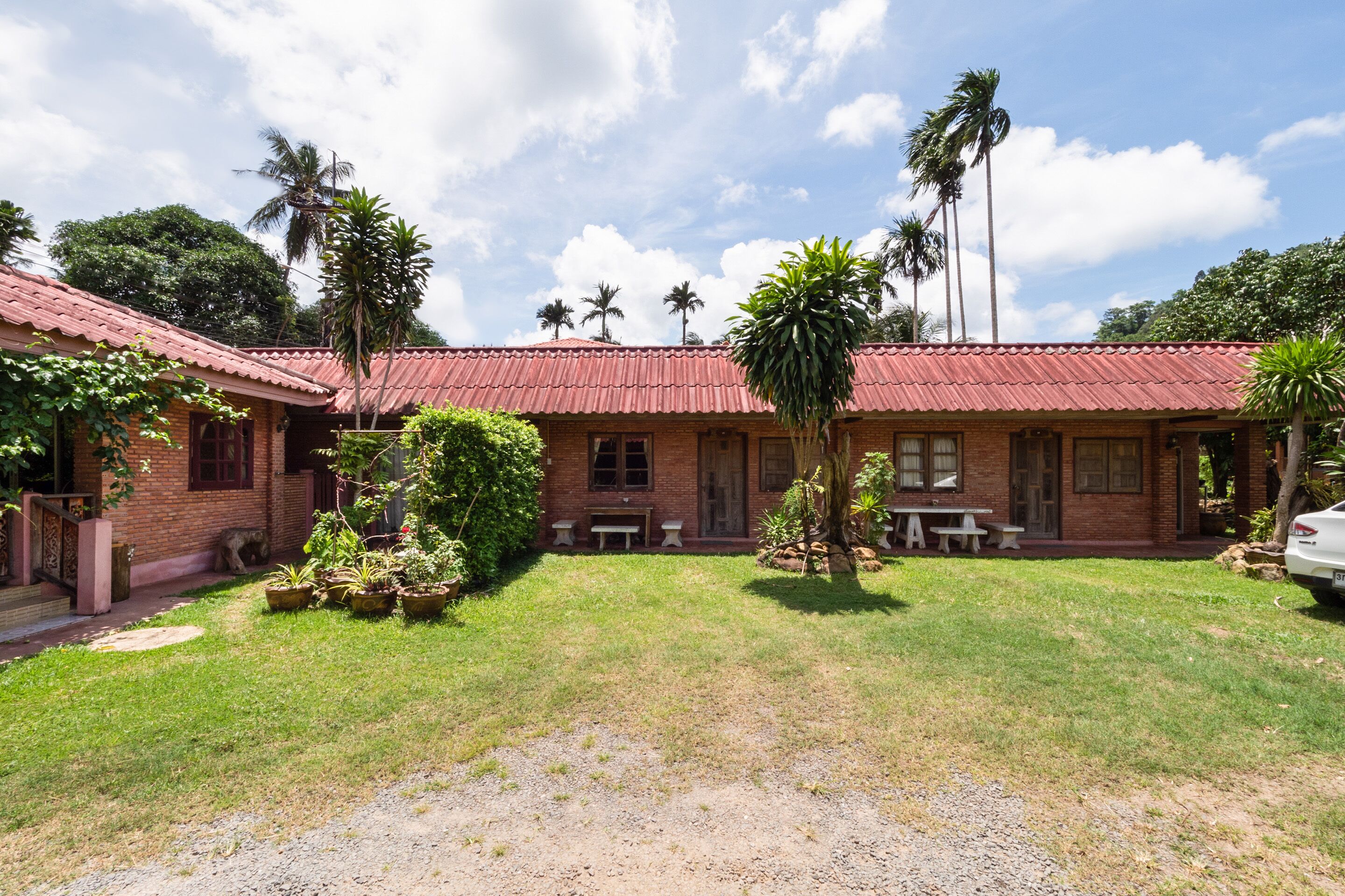 A brick building with a red roof, surrounded by a grassy lawn and palm trees.