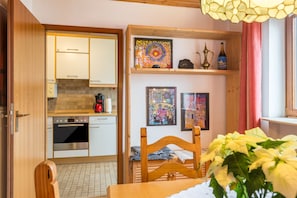 Une cuisine compacte dotée d’appareils électroménagers modernes, un coin repas avec une table et des chaises en bois, et des œuvres d’art accrochées aux murs.