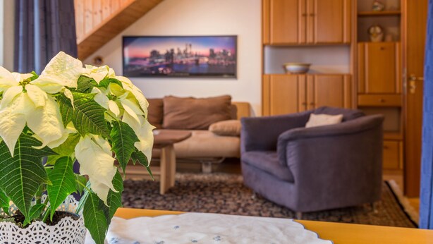 Uma sala de estar com sofá, uma mesa com um vaso de flores e uma pintura de paisagem urbana na parede.
