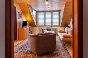 Une chambre confortable située sous les toits, avec un plafond en pente, un canapé, un fauteuil et un téléviseur.