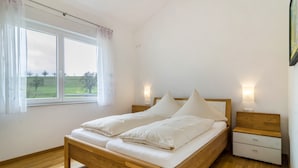 Un dormitorio con cama de madera, mesita de noche, ventana con cortinas y vista a un paisaje verde.