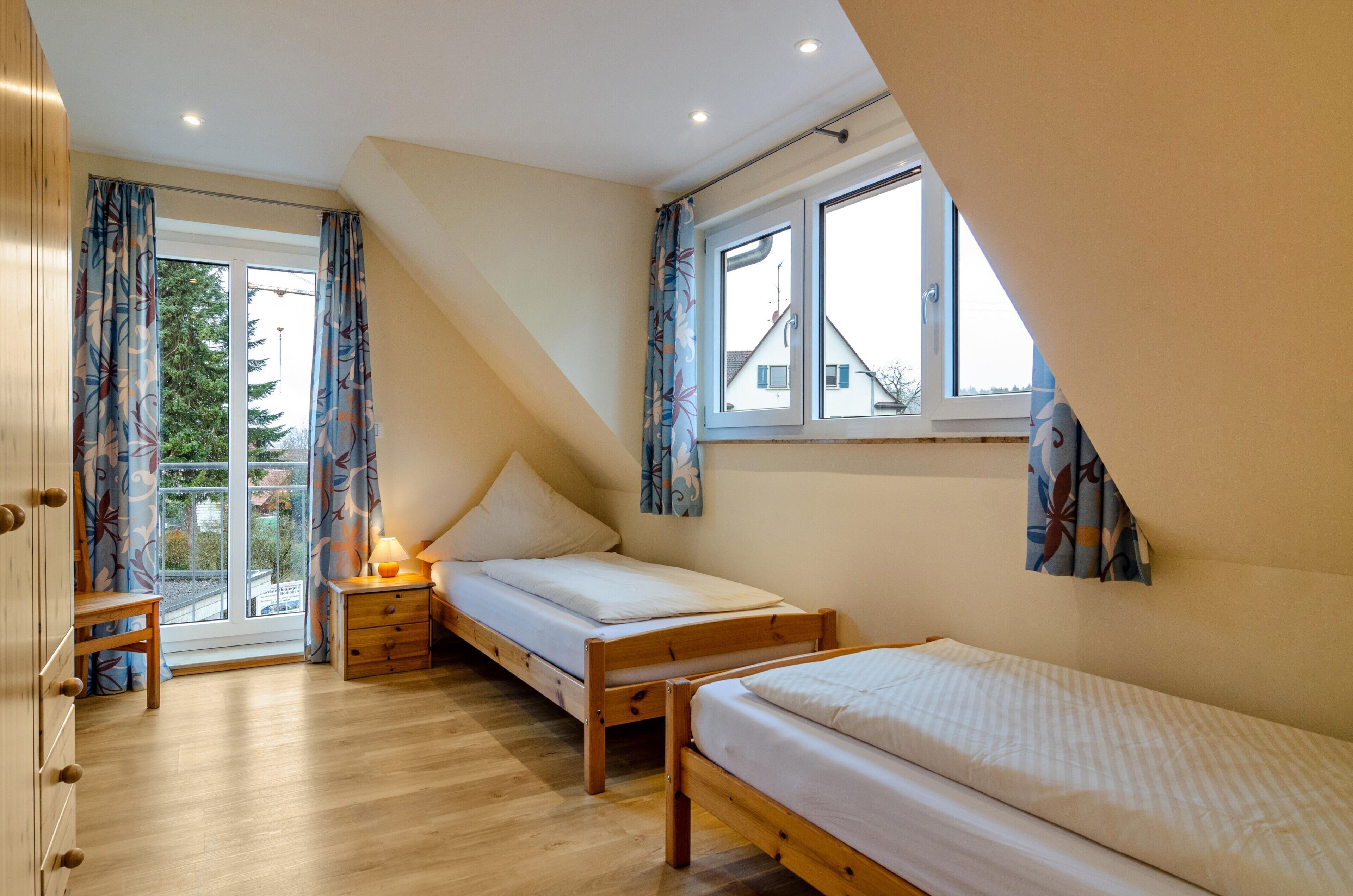 Un dormitorio con dos camas de madera, una ventana, una puerta y una mesita con una lámpara.