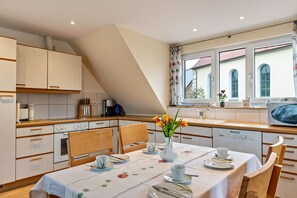 A kitchen with wooden cabinets, a dining table set with plates, cups, and a vase of flowers.